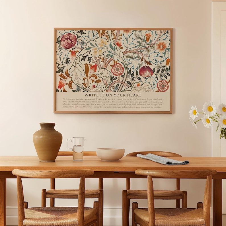 May include: A framed floral art print with a beige background and a variety of flowers in shades of red, orange, and green. The print is above a wooden table with a vase, a glass, and a bowl. The text "WRITE IT ON YOUR HEART" is at the bottom of the print.