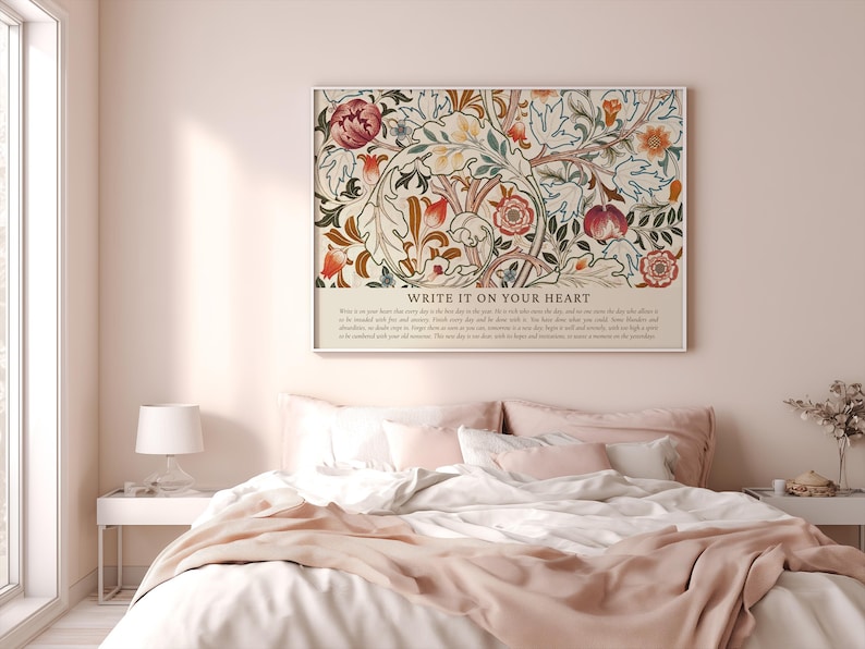 May include: A framed floral art print with the text "WRITE IT ON YOUR HEART" hangs above a bed. The artwork features a cream background with red, orange, and green floral patterns. The bed has white linens and a pink blanket.