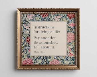 May include: A square framed wall art piece featuring a beige central panel with the black text: Instructions for living a life: Pay attention. Be astonished. Tell about it. Mary Oliver. The border displays a dark blue floral pattern.