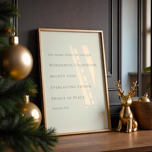 May include: A framed wall art print featuring the text: HIS NAME SHALL BE CALLED WONDERFUL COUNSELOR, MIGHTY GOD, EVERLASTING FATHER, PRINCE OF PEACE. ISAIAH 9:6. The print is encased in a thin gold frame and displayed on a wooden surface.