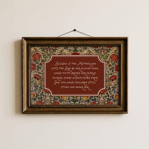 May include: A framed print with a dark brown wooden frame. The print features a burgundy-colored central panel with white text. The background has a floral pattern with red roses and green leaves. The text reads "Blessed is the Mother..."