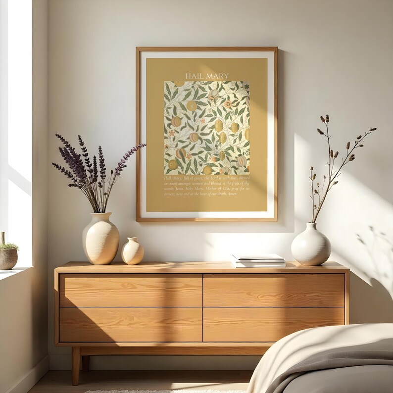 May include: A framed wall art print featuring a mustard yellow background with the text HAIL MARY at the top and the prayer text at the bottom. The center displays a rectangular botanical illustration of oranges, leaves, and flowers in muted tones.
