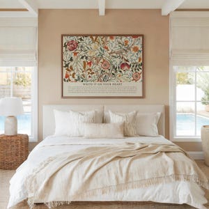 May include: A bedroom scene featuring a bed with white linens, pillows, and a beige throw blanket. Above the bed hangs a framed floral print with the text "WRITE IT ON YOUR HEART". The room has neutral tones and natural light.