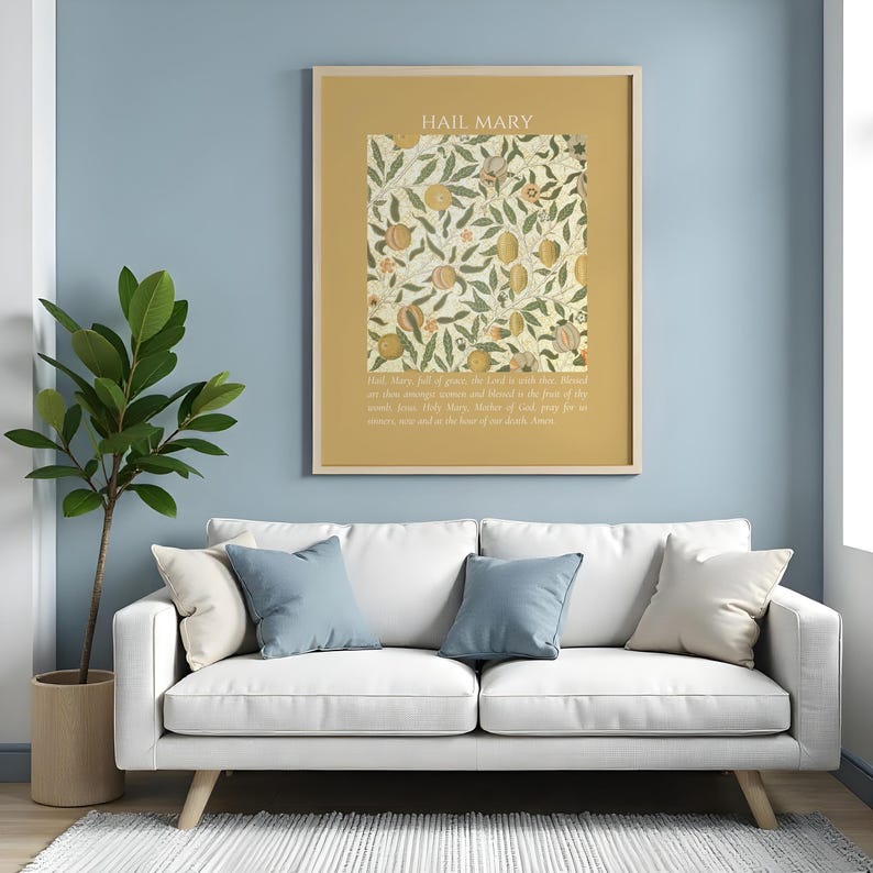 May include: A framed wall art print featuring the text HAIL MARY at the top and a prayer at the bottom, surrounding a central botanical illustration of fruits and leaves in shades of gold, green, and cream on a mustard yellow background.