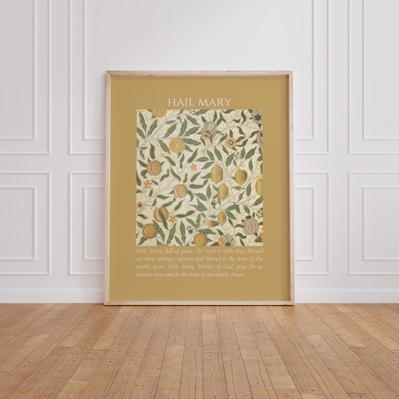 May include: A rectangular wall art print with a mustard yellow border featuring the text HAIL MARY at the top and the full prayer text at the bottom. The center displays a botanical pattern of green leaves and orange fruits on a cream background.