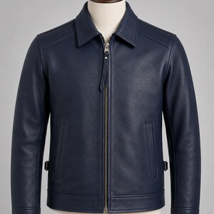 May include: A navy blue jacket with a textured finish, featuring a classic collar, a central metal zipper closure with a long pull tab, two vertical side pockets, and adjustable side straps at the hem, displayed on a neutral-toned mannequin.