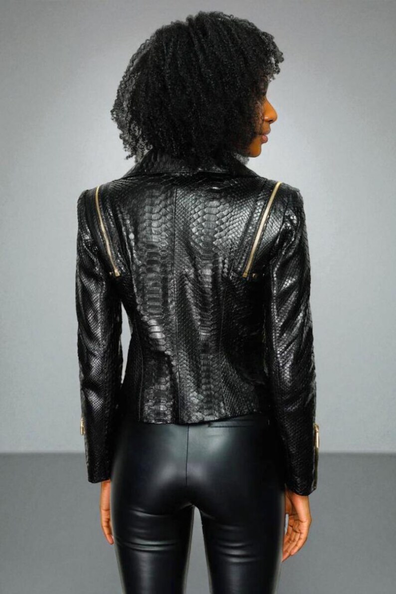 May include: A black leather jacket with a snakeskin texture and gold zippers. The jacket has a tailored fit and is worn with black leather pants. The model is facing away from the camera.