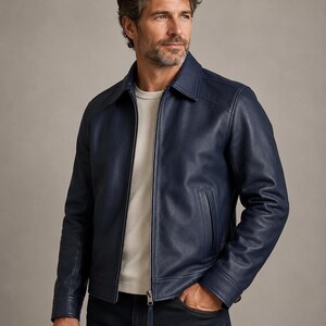 May include: A navy blue leather jacket featuring a classic collar, a full-length silver metal zipper closure, and two vertical side pockets. The jacket is worn over a plain white crew neck t-shirt and dark denim jeans, showcasing a smooth texture.