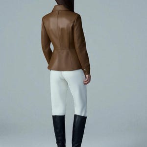 May include: A brown leather jacket with a tailored fit, featuring a collar and button details. Paired with white pants and black knee-high boots. The jacket's color is a rich, warm brown.