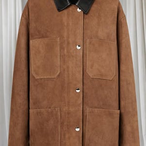 May include: A brown suede jacket with a black leather collar. The jacket has four front pockets and silver button closures. The garment is a classic style, suitable for various occasions.