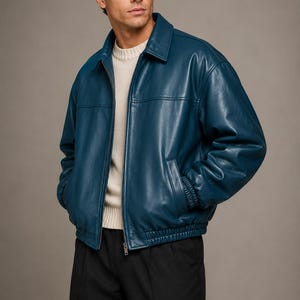May include: A teal blue leather jacket with a classic collar, a full-length front zip, and an elasticated waistband. The jacket features long sleeves with ribbed cuffs, two side pockets, and a smooth finish, worn over a cream jumper.