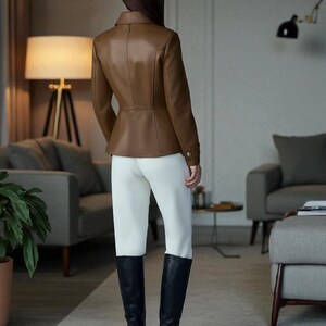 May include: A brown leather jacket with a tailored fit, paired with white pants and black knee-high boots. The jacket has a classic design with a collar and button details. The boots have a block heel.