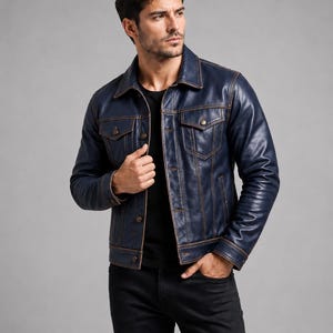 May include: A navy blue leather jacket featuring a classic collar, long sleeves with buttoned cuffs, two chest pockets with buttoned flaps, and a front button closure. The jacket is accented with visible brown stitching along the seams and pockets.