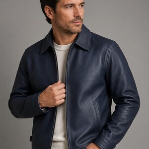 May include: A navy blue leather jacket featuring a classic collar, a full-length silver-toned front zipper, and two side pockets. The jacket is worn over a white crew-neck sweater, showcasing a smooth texture and a structured, tailored fit.