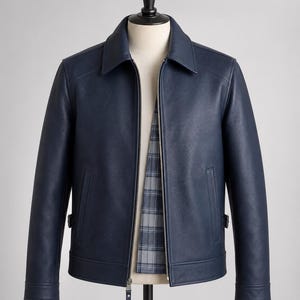 May include: A navy blue jacket with a textured finish, featuring a classic collar, a full-length silver metal zipper, and two vertical side pockets. The interior lining displays a grey and blue plaid pattern, and the cuffs have a button detail.