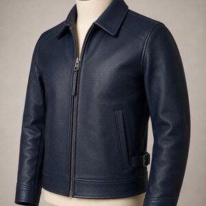 May include: A navy blue leather jacket featuring a classic collar, a full-length front metal zipper closure, long sleeves with cuffs, and a side waist adjustment strap with a metal buckle. The jacket has two vertical welt pockets at the front.