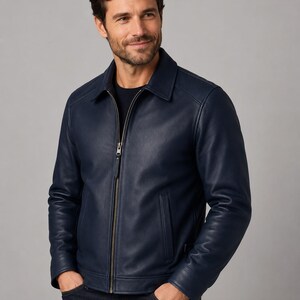 May include: A navy blue leather jacket featuring a classic collar, a full-length metal front zipper, and two vertical side pockets. The jacket has long sleeves with cuffs and a smooth, matte finish, worn over a dark shirt and dark denim jeans.