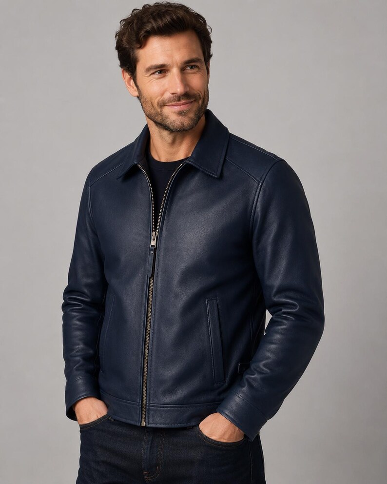 May include: A navy blue leather jacket featuring a classic collar, a full-length metal front zipper, and two vertical side pockets. The jacket has long sleeves with cuffs and a smooth, matte finish, worn over a dark shirt and dark denim jeans.