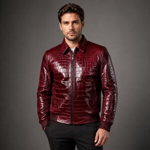 May include: A deep burgundy jacket featuring a glossy, embossed crocodile skin texture. The garment includes a classic collar, a central black zipper closure, and ribbed knit cuffs and hem. The material has a polished finish throughout.