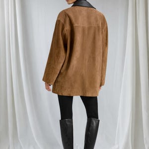 May include: A brown suede jacket with a black leather collar. The jacket is worn over black leggings and tall black boots. The model is facing away from the camera.