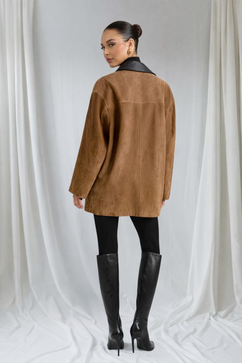 May include: A brown suede jacket with a black leather collar. The jacket is worn over black leggings and tall black boots. The model is facing away from the camera.