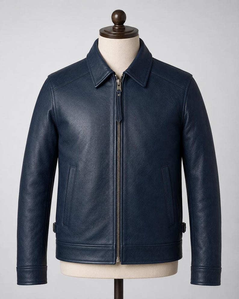 May include: A dark navy blue leather jacket featuring a classic point collar, a full-length metal front zipper with a matching leather pull tab, two vertical side pockets, and adjustable side waist tabs, displayed on a neutral mannequin torso.