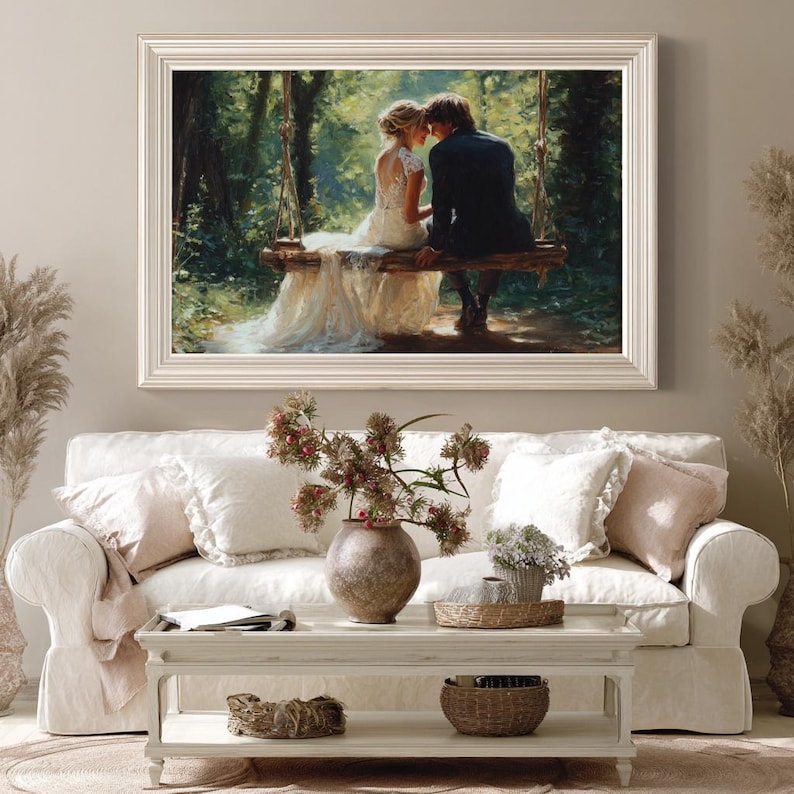 May include: A framed painting depicts a couple on a swing in a forest. The artwork is displayed above a white sofa with decorative pillows. A coffee table with a vase of flowers and other decor sits in front of the sofa.
