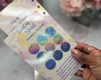 May include: A savings challenge card with the text "Fruit of the Spirit" and "Savings Challenge". The card features nine scratch-off circles with a holographic, glittery effect. The card has a floral design.