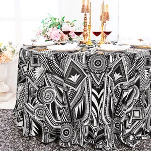 May include: Black and white geometric patterned tablecloth with a round shape. The tablecloth is set for a dinner party with wine glasses and plates.