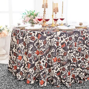 May include: A round white tablecloth with a black and orange floral pattern. The tablecloth is laid on a table with wine glasses and candlesticks.