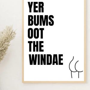 May include: A framed print with the text "YER BUMS OOT THE WINDAE" in bold black letters. A simple line drawing of a rear end is on the right. The frame is a light wood color, and the background is white.
