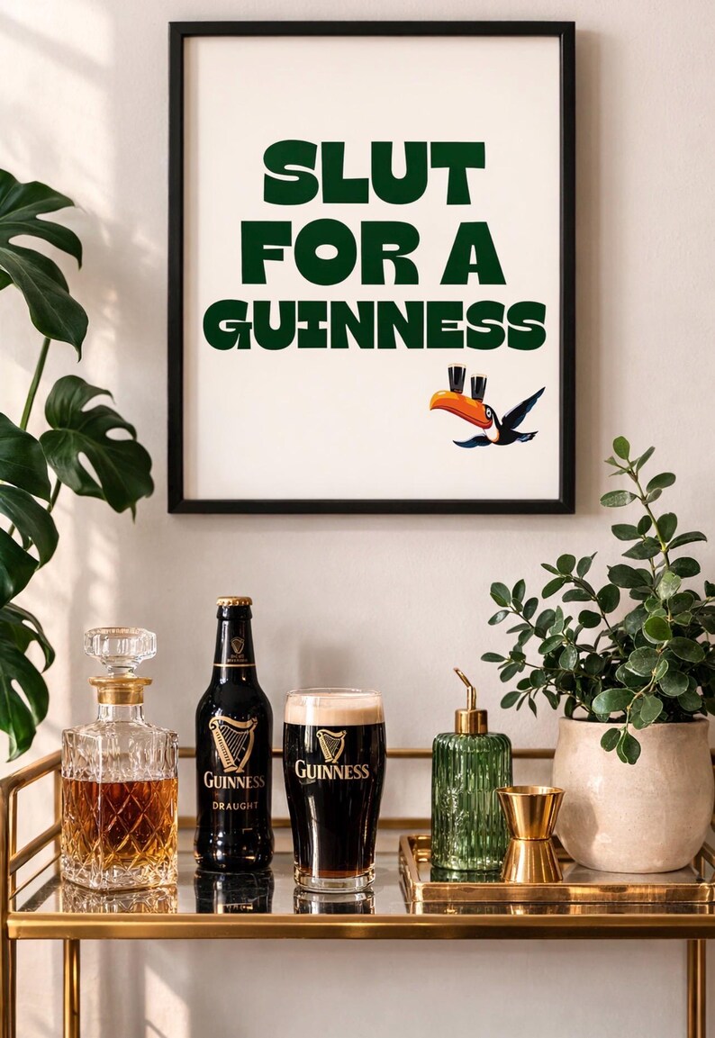 Puede incluir: Un cuadro enmarcado con el texto verde "SLUT FOR A GUINNESS" y una ilustraci&oacute;n de tuc&aacute;n. Debajo, un carrito de bar exhibe una botella de Guinness, un vaso de Guinness y una jarra, creando un ambiente de pub.