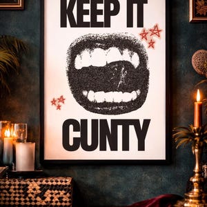 May include: Black framed art print with the words "KEEP IT" above a black, textured mouth graphic and the word "CUNTY" below. Red star stickers are placed above the mouth. The art is displayed on a dark green wall.