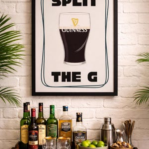 May include: A black framed print with the words "SPLIT THE G" and a Guinness pint glass graphic. The print hangs above a bar cart with bottles of spirits, glasses, a cocktail shaker, and a bowl of limes.