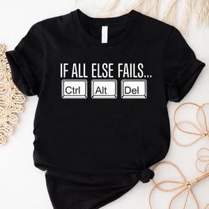 May include: Black t-shirt with the text "IF ALL ELSE FAILS..." above the Ctrl, Alt, and Del keys. The text and keys are in white. The shirt is folded at the bottom.