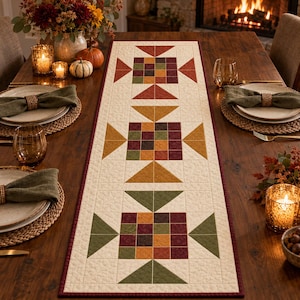 Può includere: Un runner da tavola trapuntato rettangolare con sfondo color crema, caratterizzato da tre motivi geometrici ripetuti nei toni del bordeaux, giallo senape e verde oliva, rifinito con un bordo bordeaux scuro e cuciture dettagliate.