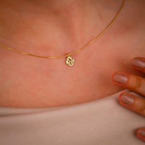 May include: A gold chain necklace with a small, round pendant featuring a monogram design.