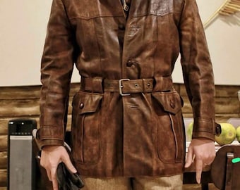 May include: A brown leather jacket with a belted waist, two front pockets, and a collared neckline. The jacket is worn with tan pants and a patterned tie. The overall style is vintage and classic.