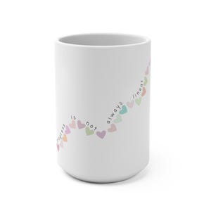 Könnte beinhalten: Weiße Keramiktasse mit einem Design aus bunten Herzen in einer geschwungenen Linie. Der Text "Progress is not always linear" ist auf der Tasse aufgedruckt.