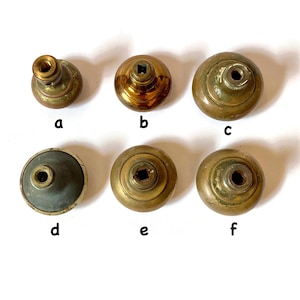 May include: A collection of six antique brass knobs, each with a unique design. The knobs vary in shape, with some featuring a rounded top and others a more cylindrical form. The brass has a warm, aged patina, suggesting vintage origins. These knobs are suitable for furniture restoration.