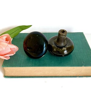 May include: Two black ceramic door knobs with a brass base. The knobs are on a green book.