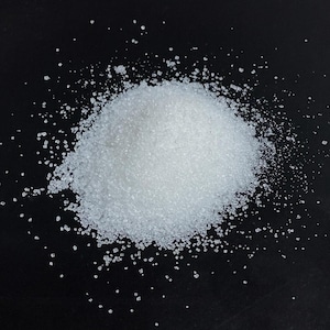 May include: A pile of white granulated sugar on a black surface.