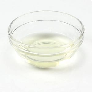 May include: A clear glass bowl filled with a pale yellow liquid. The bowl is round with a slightly flared rim and sits on a white surface. The liquid appears to be translucent.