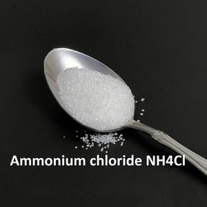 May include: A silver spoon filled with white ammonium chloride crystals, with a few crystals scattered on a black surface. The text "Ammonium chloride NH4Cl" is written below the spoon.