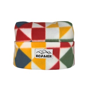 May include: A colorful fleece beanie with a geometric pattern in red, yellow, green, and blue squares. The beanie has a white label with the word "ROAMER" and a mountain graphic.