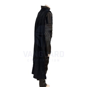 May include: A black costume with a long cape. The outfit includes a high-collared jacket with geometric and striped detailing, and dark pants. The costume is displayed on a mannequin.