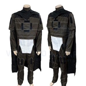 May include: A brown costume with black accents, featuring a high collar, cape, and a white panel at the waist. The outfit includes a jacket with square patches and matching pants. The costume is displayed on a mannequin.