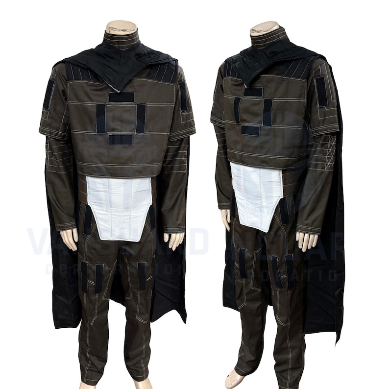 May include: A brown costume with black accents, featuring a high collar, cape, and a white panel at the waist. The outfit includes a jacket with square patches and matching pants. The costume is displayed on a mannequin.