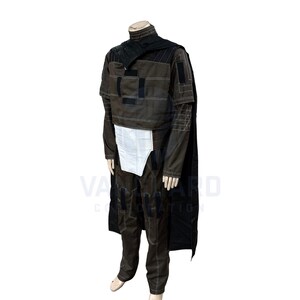 May include: A full-body costume with a brown jacket, pants, and a black cape. The jacket has black patches and white stitching. A white panel is visible at the waist. The costume is displayed on a mannequin.