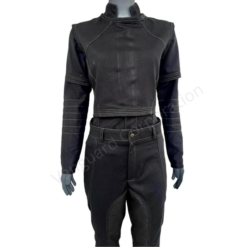 Puede incluir: Una blusa negra de manga larga con cuello alto y costuras blancas. La blusa es corta y tiene una silueta ajustada. Los pantalones son negros con costuras blancas y pierna recta.